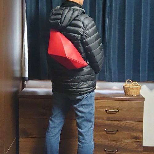 黒のダウンジャケットを着た男性が背中にレザーボディバッグ メンズ用REDを着用している写真