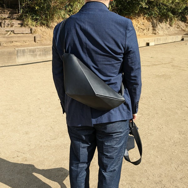 紺色のジャケットを着た男性が背中にレザーボディバッグ メンズ用BLACKを着用している写真