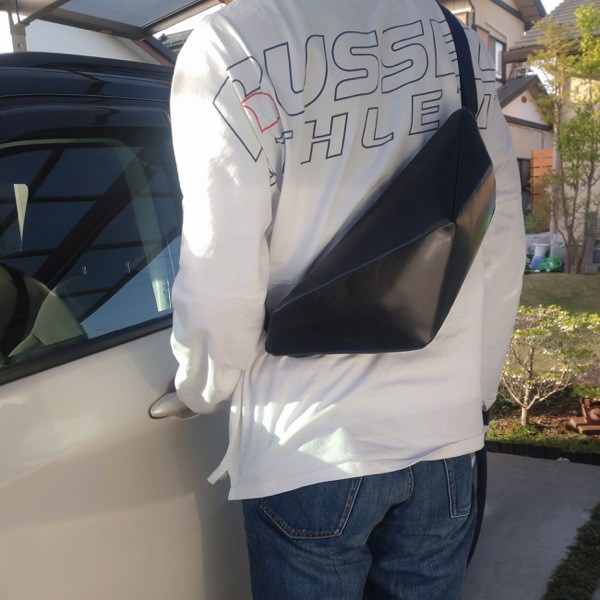 車の横に立っている男性が背中にレザーボディバッグ メンズ用CRISTAL NAVYを着用している写真