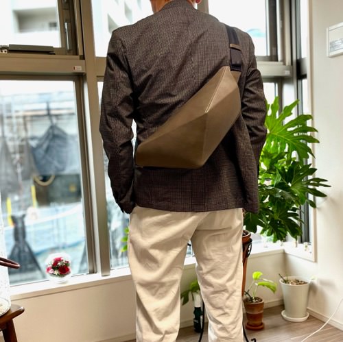 ジャケットを着た男性が背中にレザーボディバッグ メンズ用GRAYを着用している写真