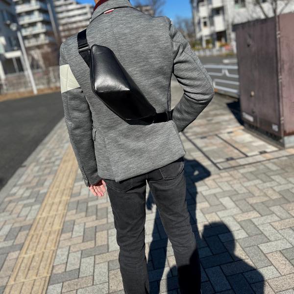 グレーのジャケットを着た男性が背中にレザーボディバッグ メンズ用CRISTAL BLACKを着用している写真