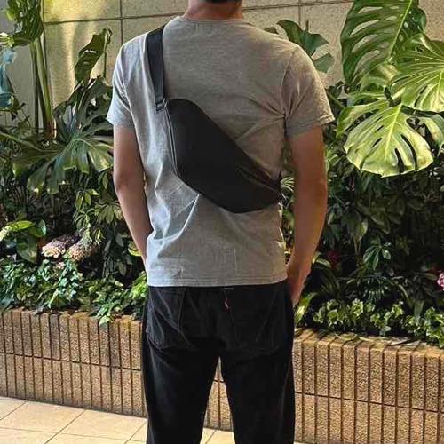 Tシャツを着た男性が背中にレザーボディバッグ メンズ用CRISTAL BLACKを着用している写真