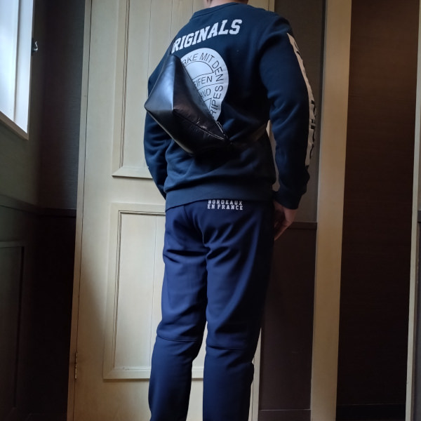 上下ジャージを着た男性が背中にレザーボディバッグ メンズ用CRISTAL BLACKを着用している写真