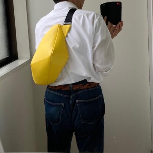 白のカッターシャツを着た男性が背中にレザーボディバッグ メンズ用YELLOWを着用している写真